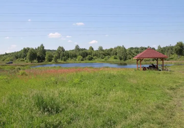 Malownicze jezioro krasowe otoczone zielenią, z altanką i rowerem przy brzegu.