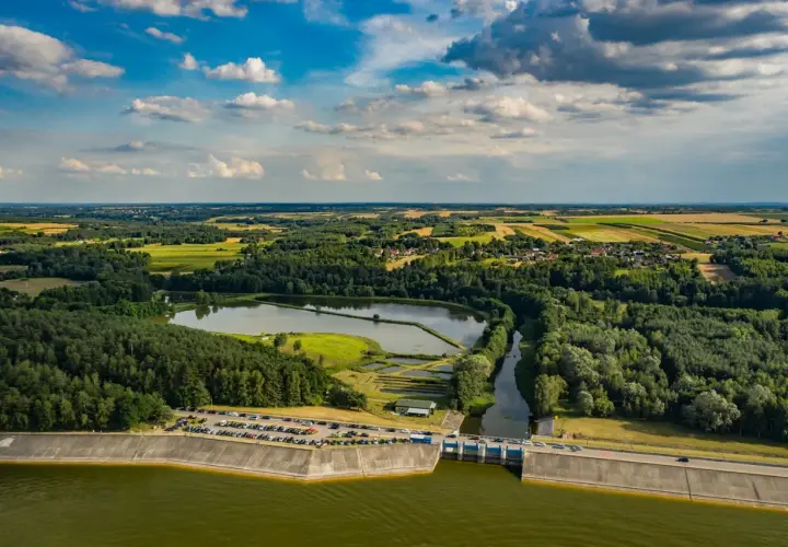 Malowniczy krajobraz z tamą i zbiornikiem wodnym. Jezioro Chańcza otoczone lasami i polami, z widoczną drogą na koronie zapory.