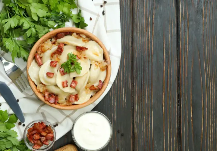 Pyszne pierogi z boczkiem i cebulką, serwowane w drewnianej misie. To kwintesencja kuchni łemkowskiej, podane z kwaśną śmietaną i świeżą natką pietruszki.