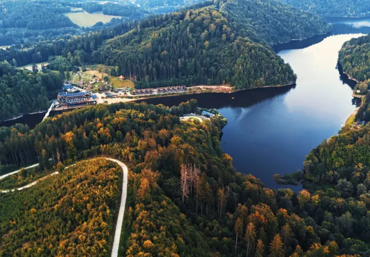 Malownicze jezioro Bystrzyckie otoczone lasami, z krętą drogą wijącą się po zboczu i zabudowaniami nad brzegiem.