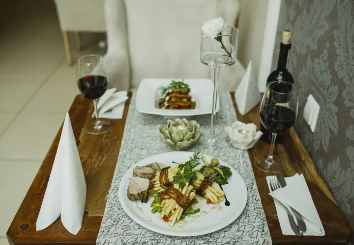 Elegancka kolacja we dwoje w Opolu. Dwa talerze z wykwintnym jedzeniem, kieliszki z czerwonym winem i świece tworzą romantyczny nastrój. Idealne opole atrakcje dla par.