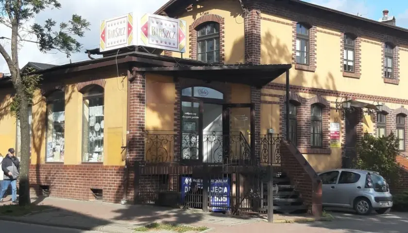 Bar "Barszcz" w Wejherowie. Żółty budynek z ceglanymi zdobieniami, szyldem "Barszcz" i małym srebrnym samochodem.