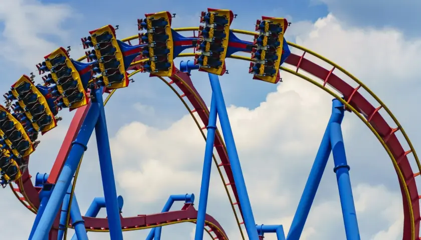 Wagoniki najwyższego rollercoastera na świecie pędzą po czerwono-żółtych torach na tle błękitnego nieba z chmurami.