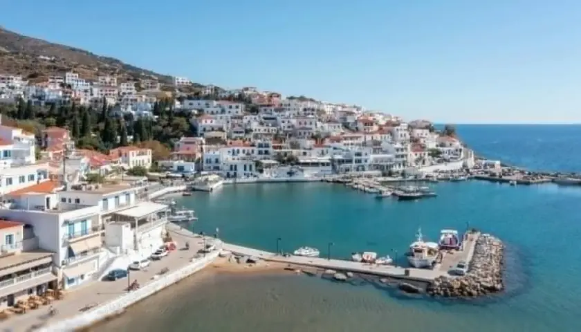 Malowniczy port na wyspie Andros, z białymi domkami wznoszącymi się na wzgórzu i błękitnym morzem.