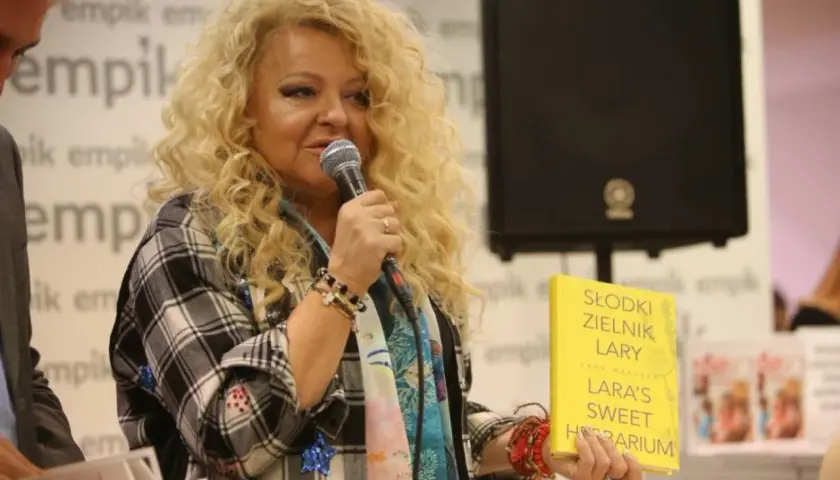 Kobieta z burzą blond włosów, trzymająca książkę "Słodki zielnik Lary", mówi do mikrofonu. Czy zajazd babski istnieje?