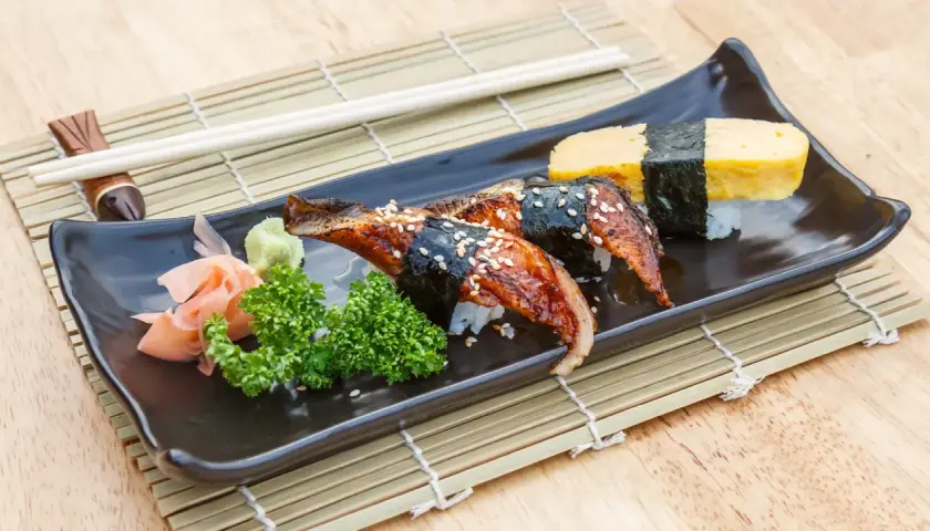 Wyśmienite unagi sushi z sezamem, podane z wasabi, imbirem i natką pietruszki na czarnej tacce.