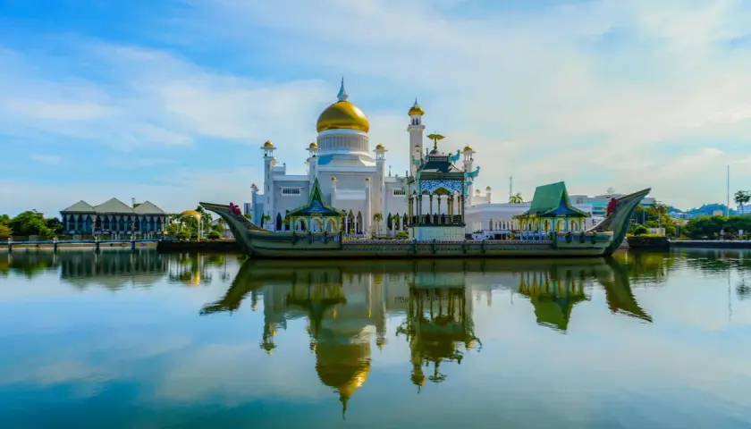 Złota kopuła meczetu Omar Ali Saifuddien w Brunei odbija się w spokojnej wodzie. Obok unosi się ozdobna łódź.