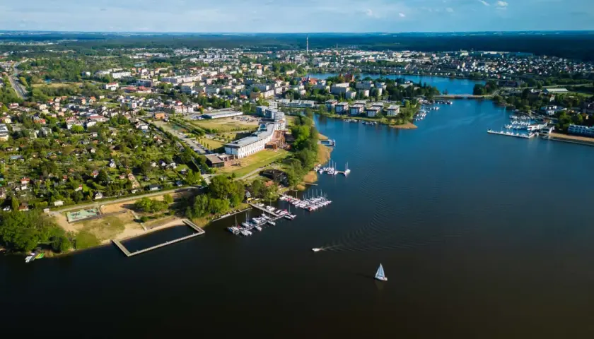 Malownicze miasto nad Jeziorakiem, z mariną pełną żaglówek i łodzi, otoczone zielenią i zabudową mieszkalną.