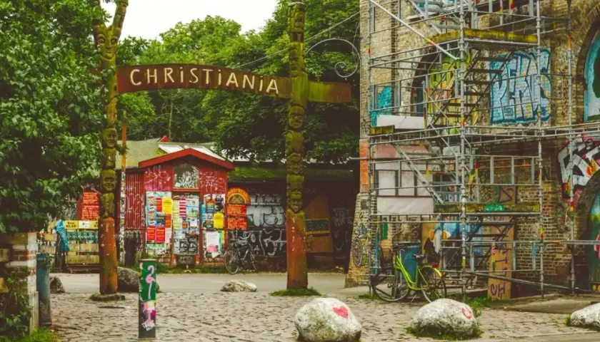 Drewniany totem i tablica z napisem CHRISTIANIA witają w wolnym mieście. Kolorowe budynki i rowery tworzą niepowtarzalny klimat.