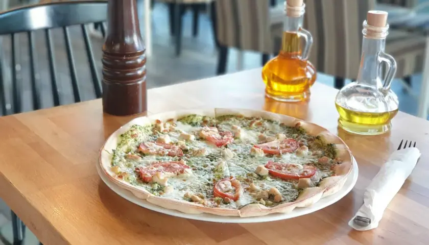 Pyszna pizza z kurczakiem i pomidorami, idealna dla szukających bezglutenowych restauracji. Na stole oliwa i przyprawnik.