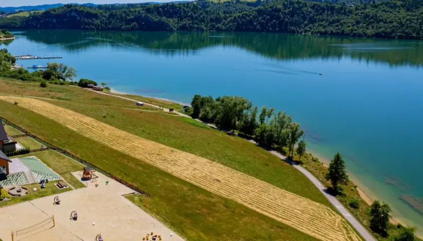 Malownicze jezioro czorsztyńskie z widokiem na domki, plac zabaw i plażę. Idealne miejsce na wypoczynek i odkrywanie atrakcji.
