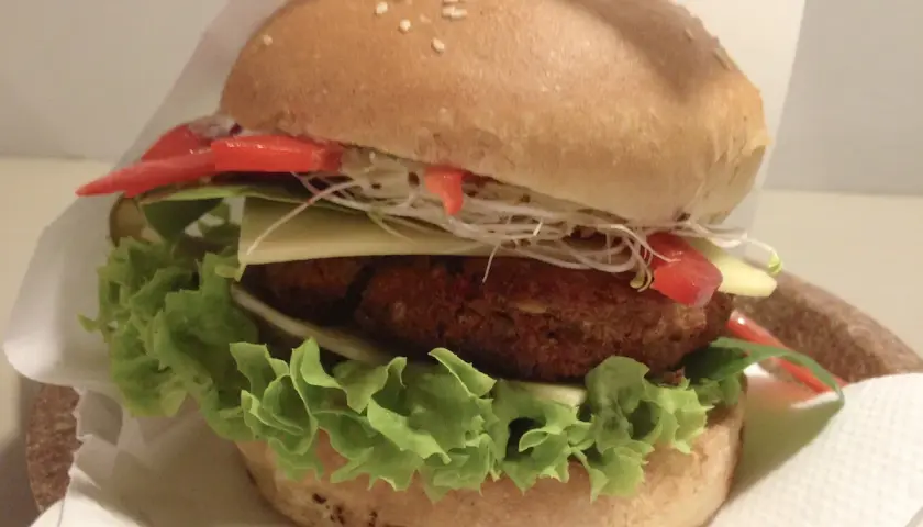 Pyszny burger z Krowarzywa Kraków: soczysty kotlet roślinny, świeża sałata, ser, pomidor i kiełki w miękkiej bułce.