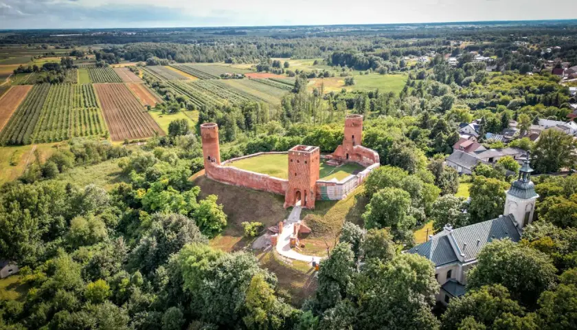 Ruiny zamku w krajobrazie rolniczym, otoczone lasem. To malownicze miejsce znajduje się w województwie mazowieckim, największym województwie w Polsce.
