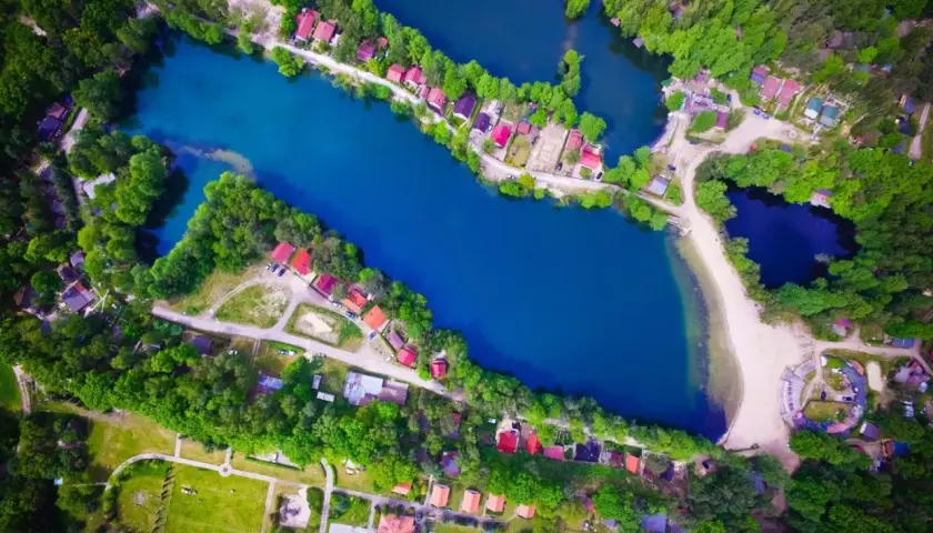 Malownicze rokitki jezioro otoczone lasem i domkami z czerwonymi dachami. Woda lśni błękitem, a plaża zaprasza do odpoczynku.