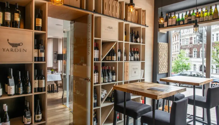 Wnętrze restauracji Muga z regałami pełnymi win, drewnianymi stołami i krzesłami barowymi.
