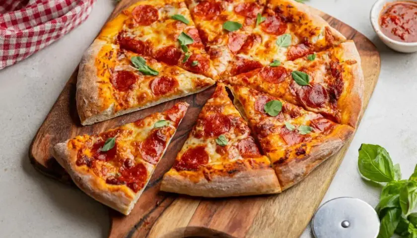 Pyszna pizza z peperoni, ciągnącym serem i świeżą bazylią, pokrojona na kawałki na drewnianej desce.
