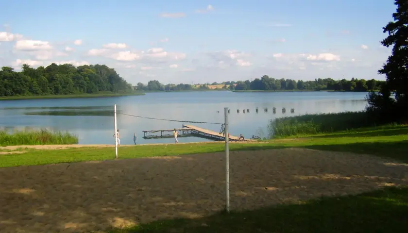 Piękny dzień nad jeziorem Skiertąg. Piaskowa plaża, pomost i zielone drzewa tworzą sielski krajobraz.