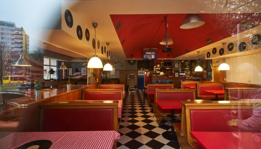 Wnętrze w stylu retro z czerwonymi kanapami i czarno-białą podłogą w szachownicę. W tle widać jukebox i dekoracje z płyt winylowych, idealne dla Queens Street Bar.