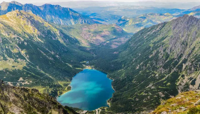 Widok z góry na Morskie Oko, jakby z kamery na żywo. Turkusowa tafla jeziora otoczona zielonymi zboczami Tatr.