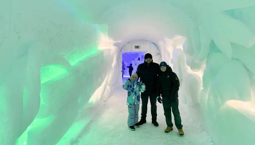 Rodzina w lodowym tunelu, który wygląda jak wejście do wioski Świętego Mikołaja. Ściany są oświetlone na zielono.
