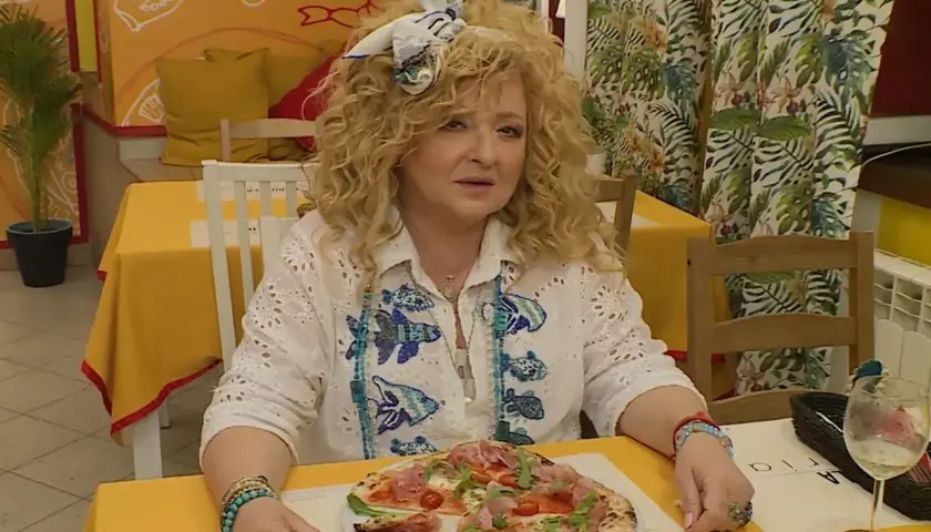 Kobieta z kręconymi włosami siedzi przy stoliku w bistro. Przed nią pizza, a za nią dekoracje ścienne. To idealne miejsce na bistro schadzka przy piecu.