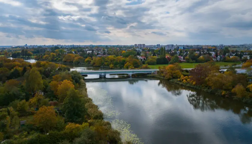 Jesioro Czerniakowskie w jesiennej szacie, z mostem i panoramą miasta w tle.
