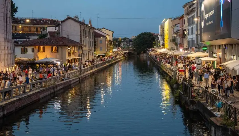 Wieczór nad kanałami Navigli w Mediolanie. Tłumy ludzi spacerują wzdłuż wody, siedzą w kawiarniach i restauracjach.