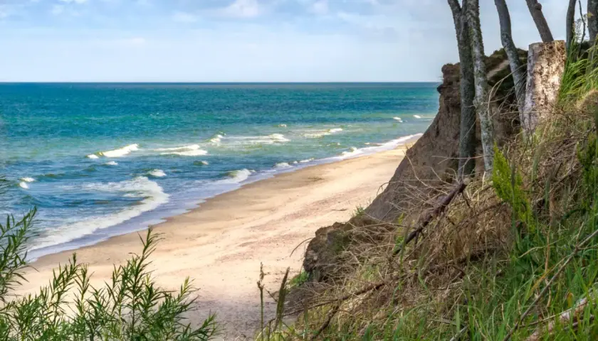 Spokojne miejsca nad morzem: piaszczysta plaża, turkusowe fale i klif porośnięty drzewami. Idealne na relaks.