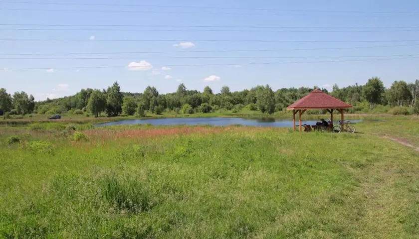 Malownicze jezioro krasowe otoczone zielenią, z altanką i rowerem przy brzegu.