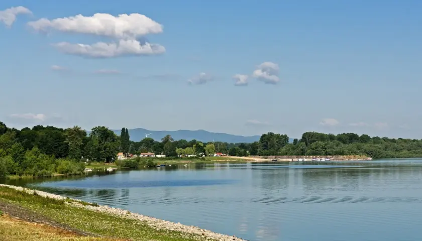 Spokojne otmuchów jezioro z łodziami przy brzegu, otoczone zielonymi drzewami i górami w tle.