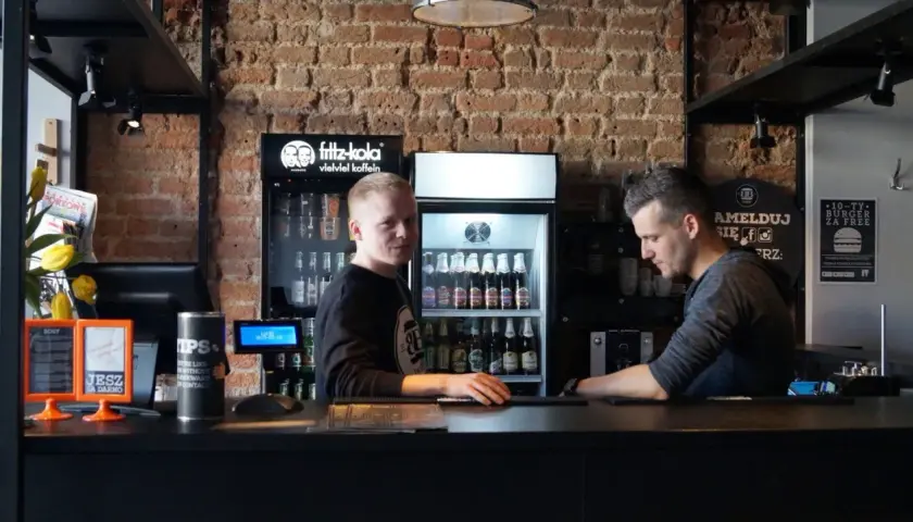 Pracownicy w Bobby Burger Bydgoszcz za ladą, obok lodówki z napojami i ekspresu do kawy.