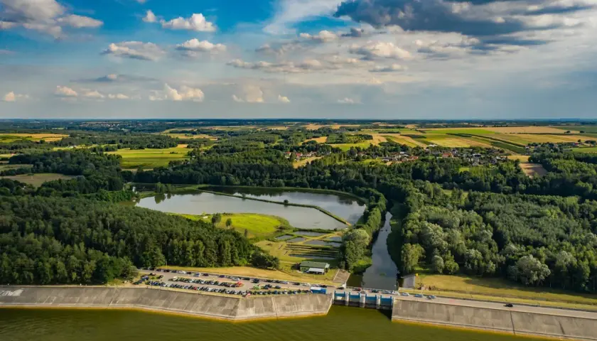 Malowniczy krajobraz z tamą i zbiornikiem wodnym. Jezioro Chańcza otoczone lasami i polami, z widoczną drogą na koronie zapory.