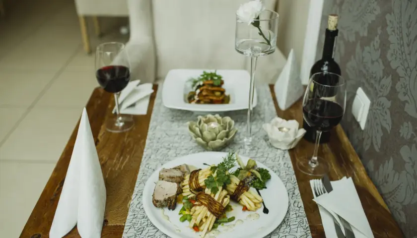 Elegancka kolacja we dwoje w Opolu. Dwa talerze z wykwintnym jedzeniem, kieliszki z czerwonym winem i świece tworzą romantyczny nastrój. Idealne opole atrakcje dla par.