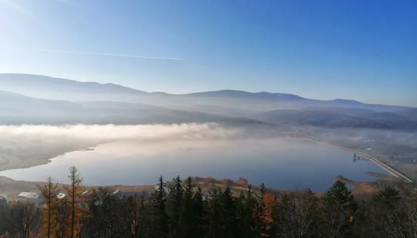 Mglisty poranek nad zbiornikiem Sosnówka. W oddali góry, a na pierwszym planie jesienny las.