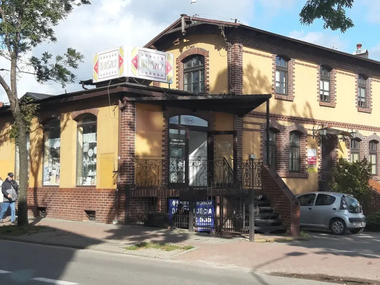 Bar "Barszcz" w Wejherowie. Żółty budynek z ceglanymi zdobieniami, szyldem "Barszcz" i małym srebrnym samochodem.