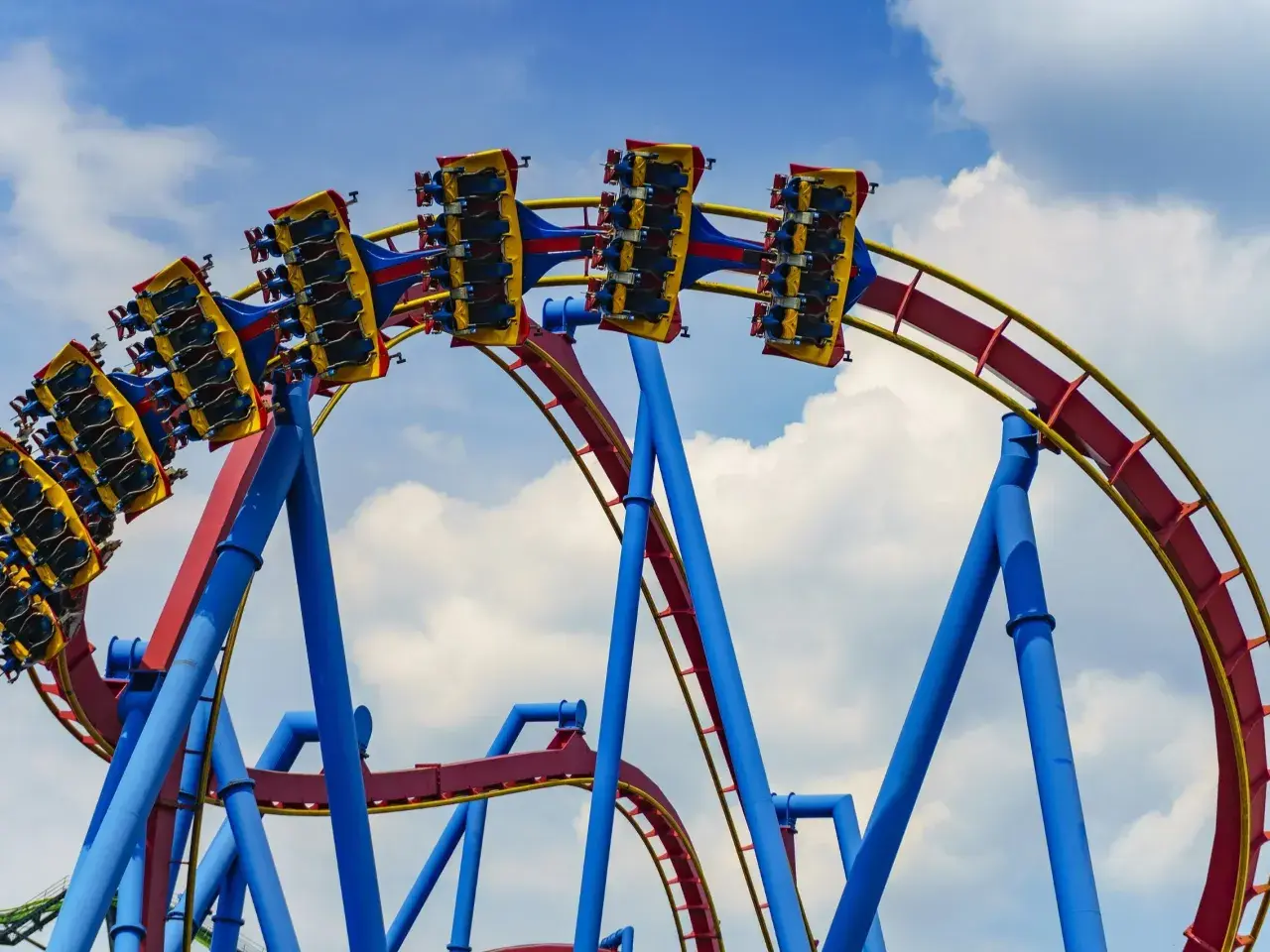 Wagoniki najwyższego rollercoastera na świecie pędzą po czerwono-żółtych torach na tle błękitnego nieba z chmurami.