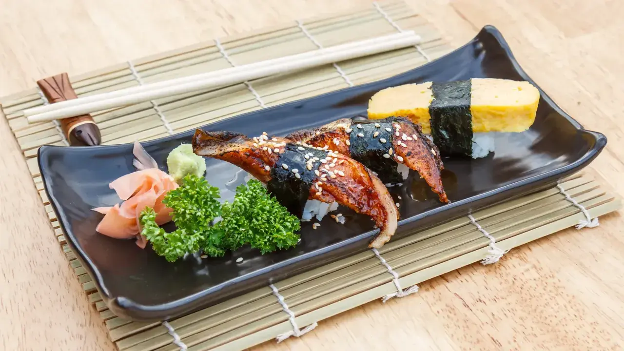 Wyśmienite unagi sushi z sezamem, podane z wasabi, imbirem i natką pietruszki na czarnej tacce.