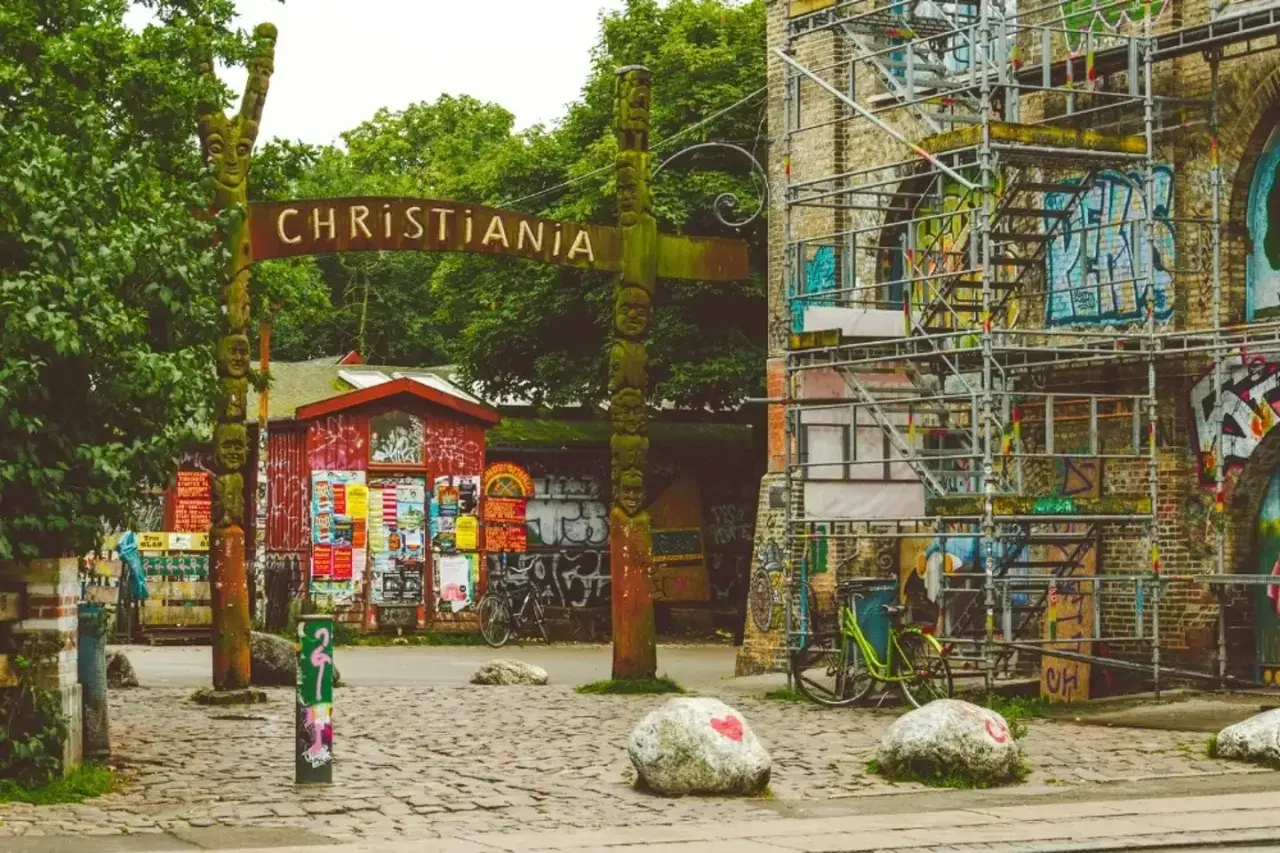 Drewniany totem i tablica z napisem CHRISTIANIA witają w wolnym mieście. Kolorowe budynki i rowery tworzą niepowtarzalny klimat.