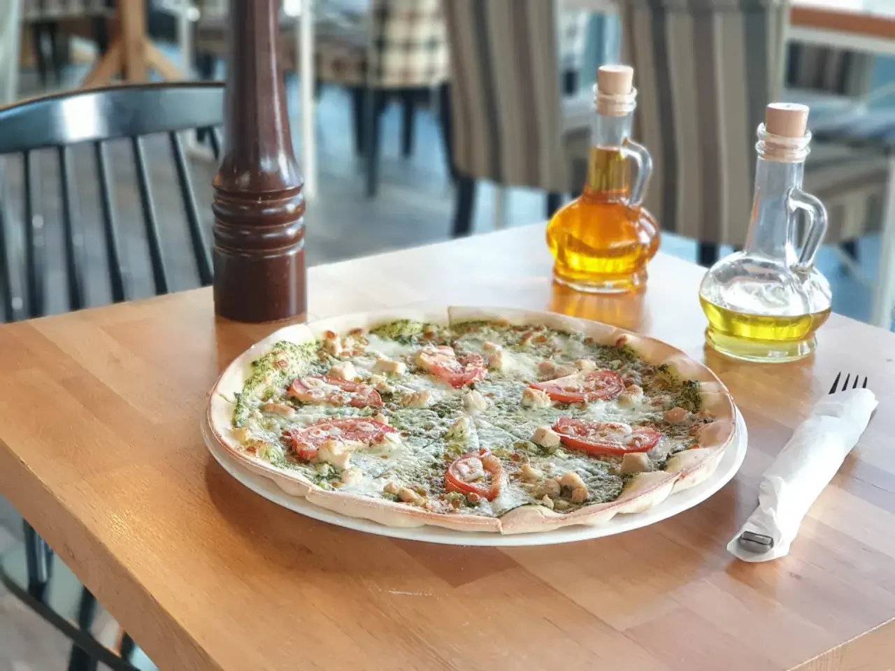 Pyszna pizza z kurczakiem i pomidorami, idealna dla szukających bezglutenowych restauracji. Na stole oliwa i przyprawnik.