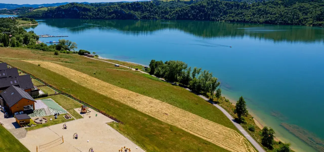 Malownicze jezioro czorsztyńskie z widokiem na domki, plac zabaw i plażę. Idealne miejsce na wypoczynek i odkrywanie atrakcji.