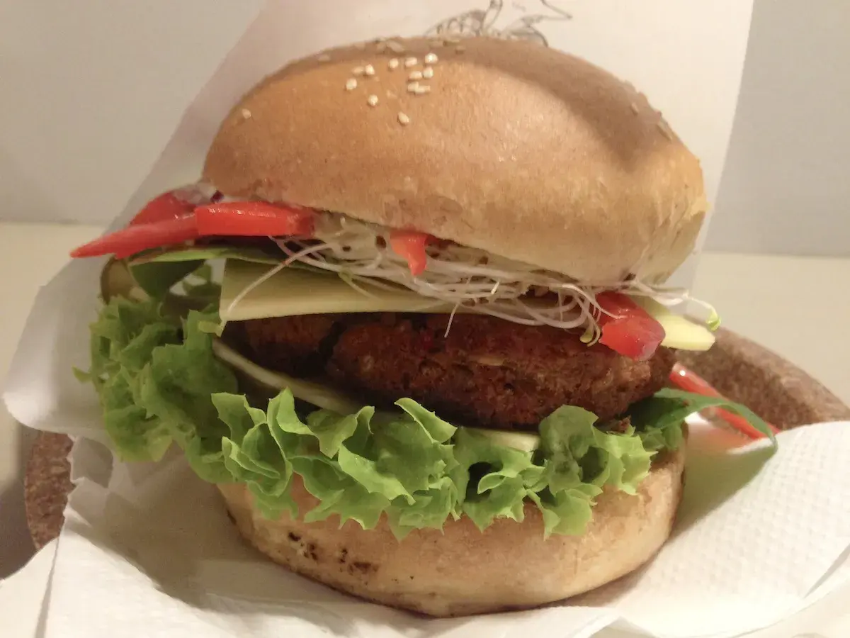 Pyszny burger z Krowarzywa Kraków: soczysty kotlet roślinny, świeża sałata, ser, pomidor i kiełki w miękkiej bułce.