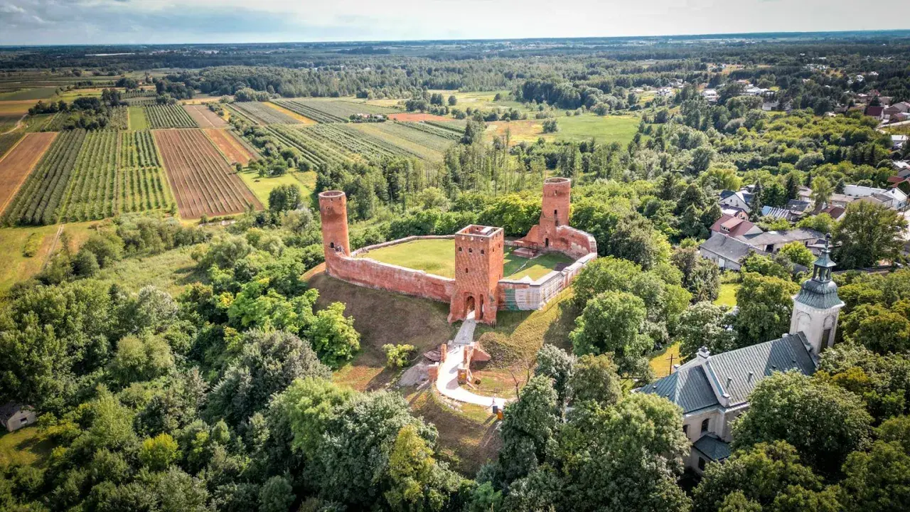 Ruiny zamku w krajobrazie rolniczym, otoczone lasem. To malownicze miejsce znajduje się w województwie mazowieckim, największym województwie w Polsce.