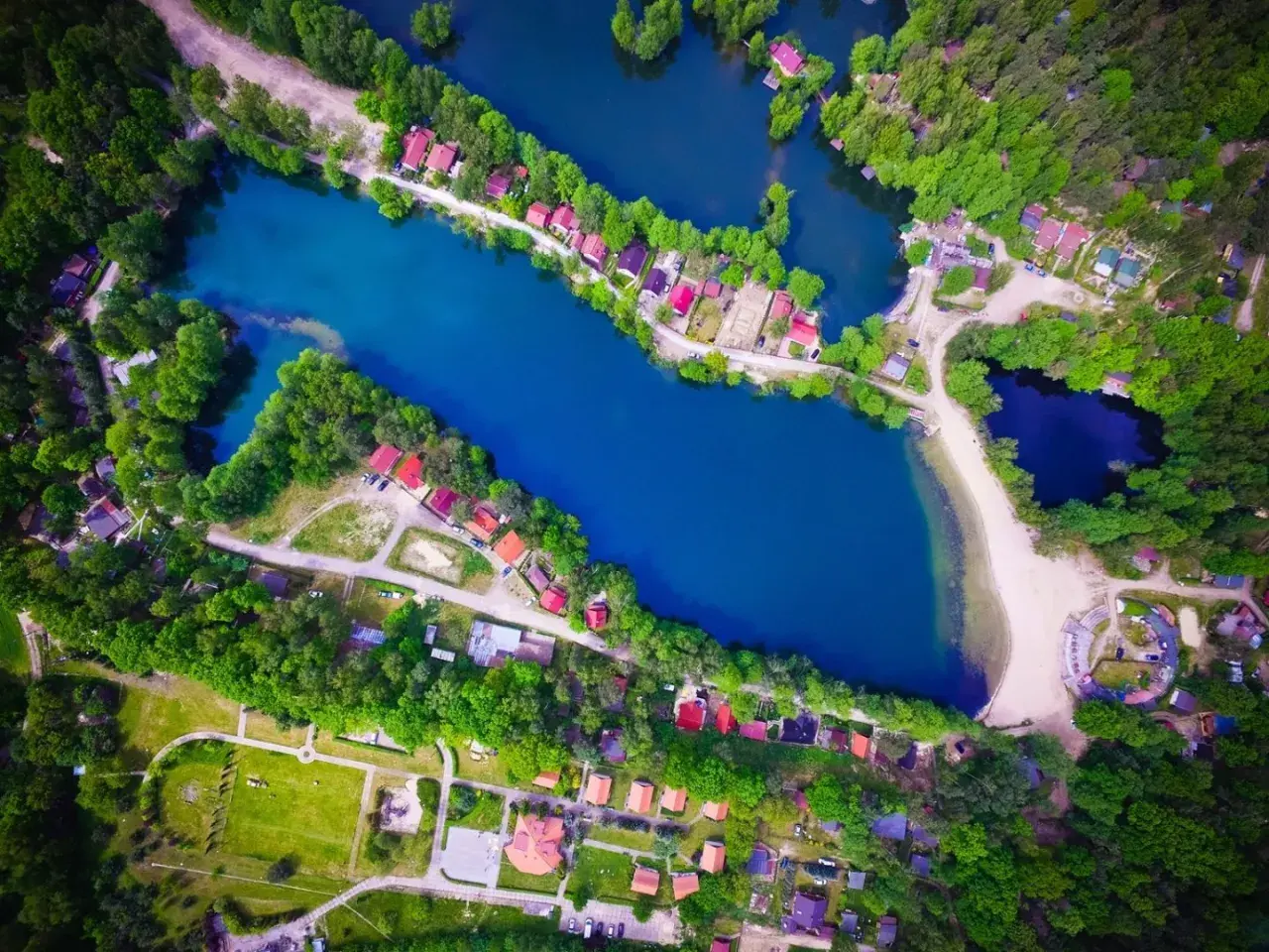 Malownicze rokitki jezioro otoczone lasem i domkami z czerwonymi dachami. Woda lśni błękitem, a plaża zaprasza do odpoczynku.