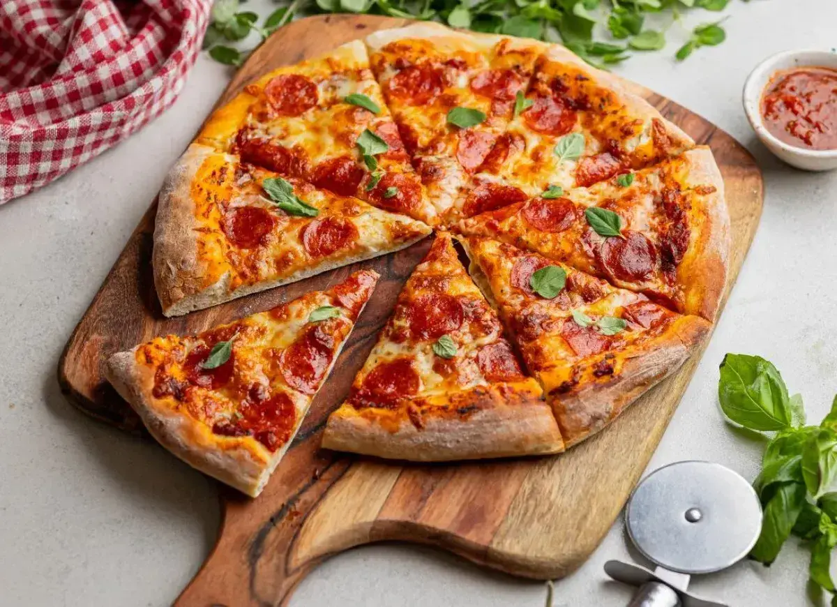 Pyszna pizza z peperoni, ciągnącym serem i świeżą bazylią, pokrojona na kawałki na drewnianej desce.
