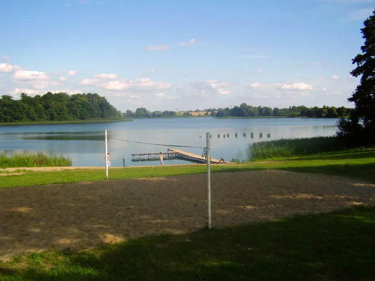 Piękny dzień nad jeziorem Skiertąg. Piaskowa plaża, pomost i zielone drzewa tworzą sielski krajobraz.