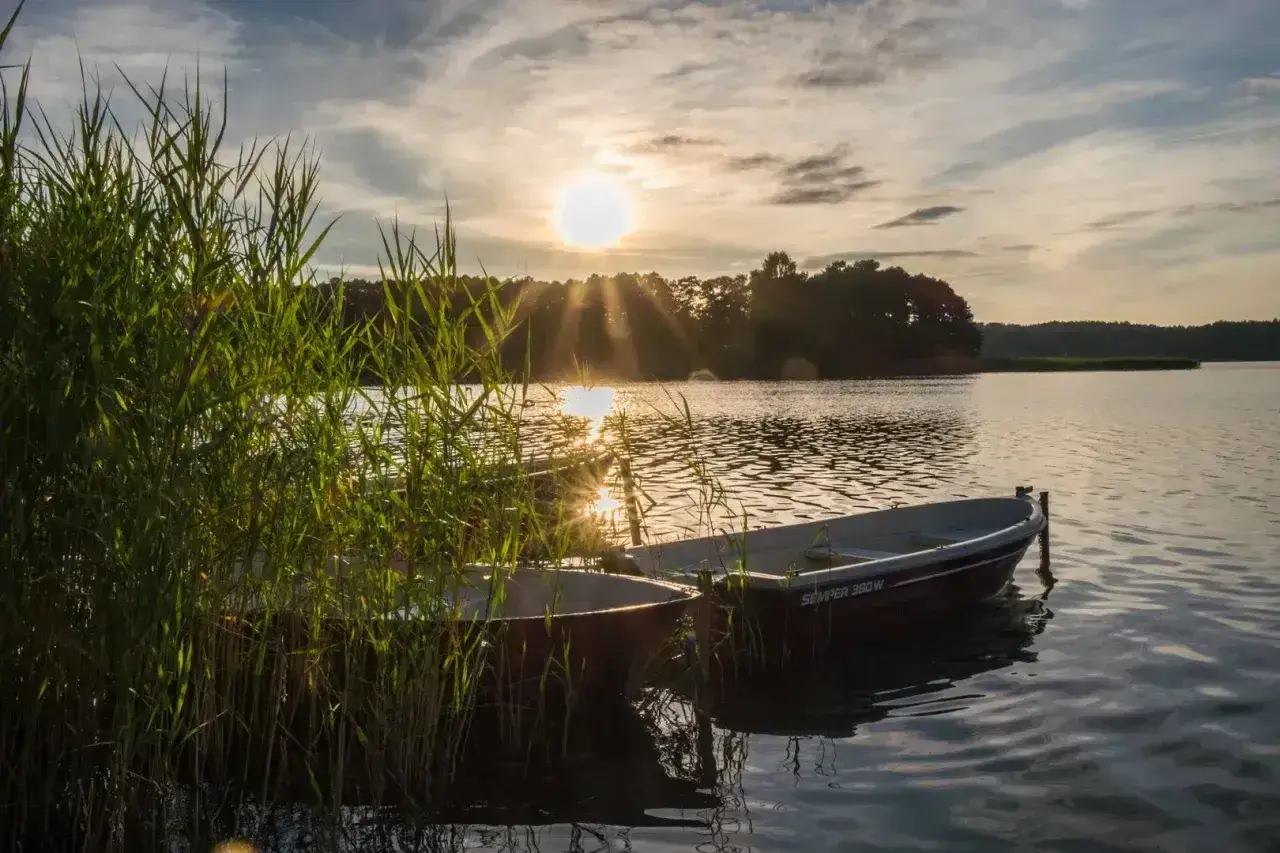 Dwa łodzie przy brzegu jeziora Świętajno, w blasku zachodzącego słońca.
