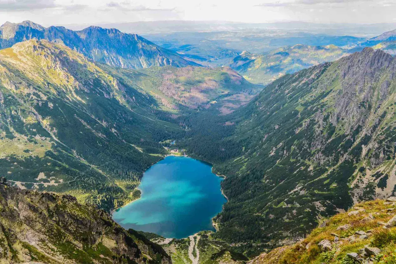 Widok z góry na Morskie Oko, jakby z kamery na żywo. Turkusowa tafla jeziora otoczona zielonymi zboczami Tatr.