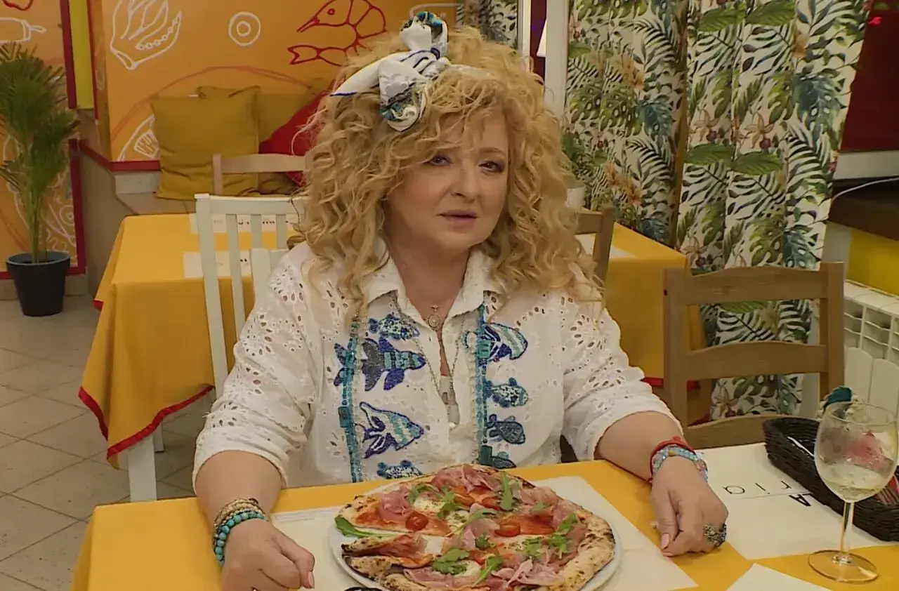 Kobieta z kręconymi włosami siedzi przy stoliku w bistro. Przed nią pizza, a za nią dekoracje ścienne. To idealne miejsce na bistro schadzka przy piecu.