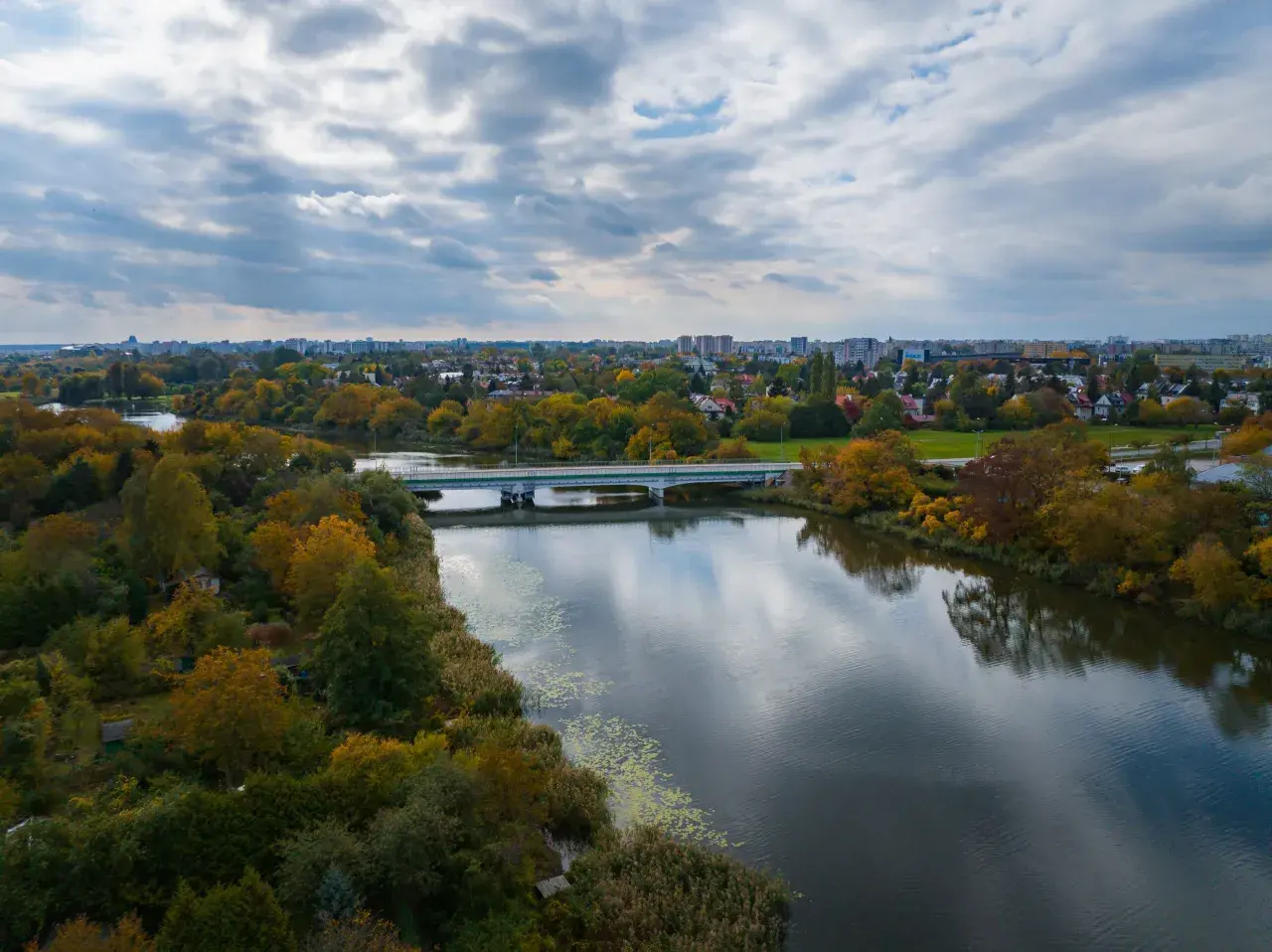 Jesioro Czerniakowskie w jesiennej szacie, z mostem i panoramą miasta w tle.