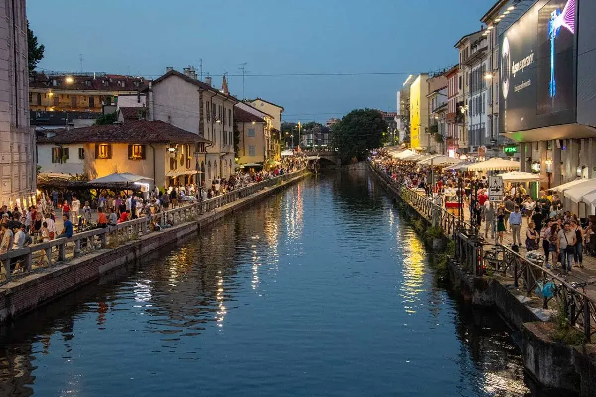 Wieczór nad kanałami Navigli w Mediolanie. Tłumy ludzi spacerują wzdłuż wody, siedzą w kawiarniach i restauracjach.